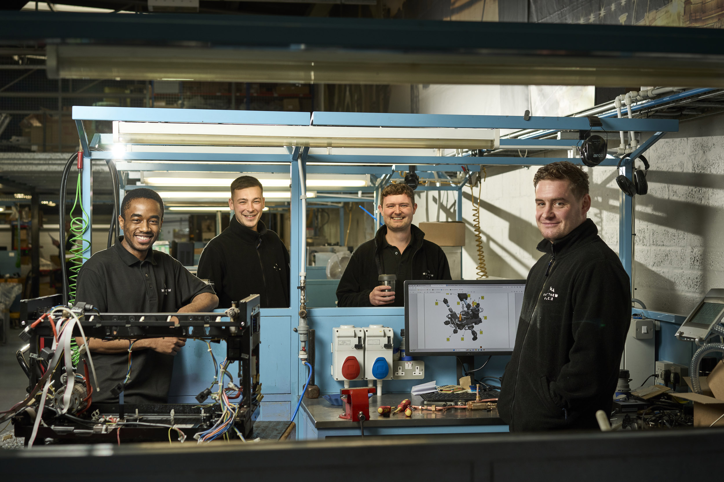 Four young coffee machine engineers posing at their work stations