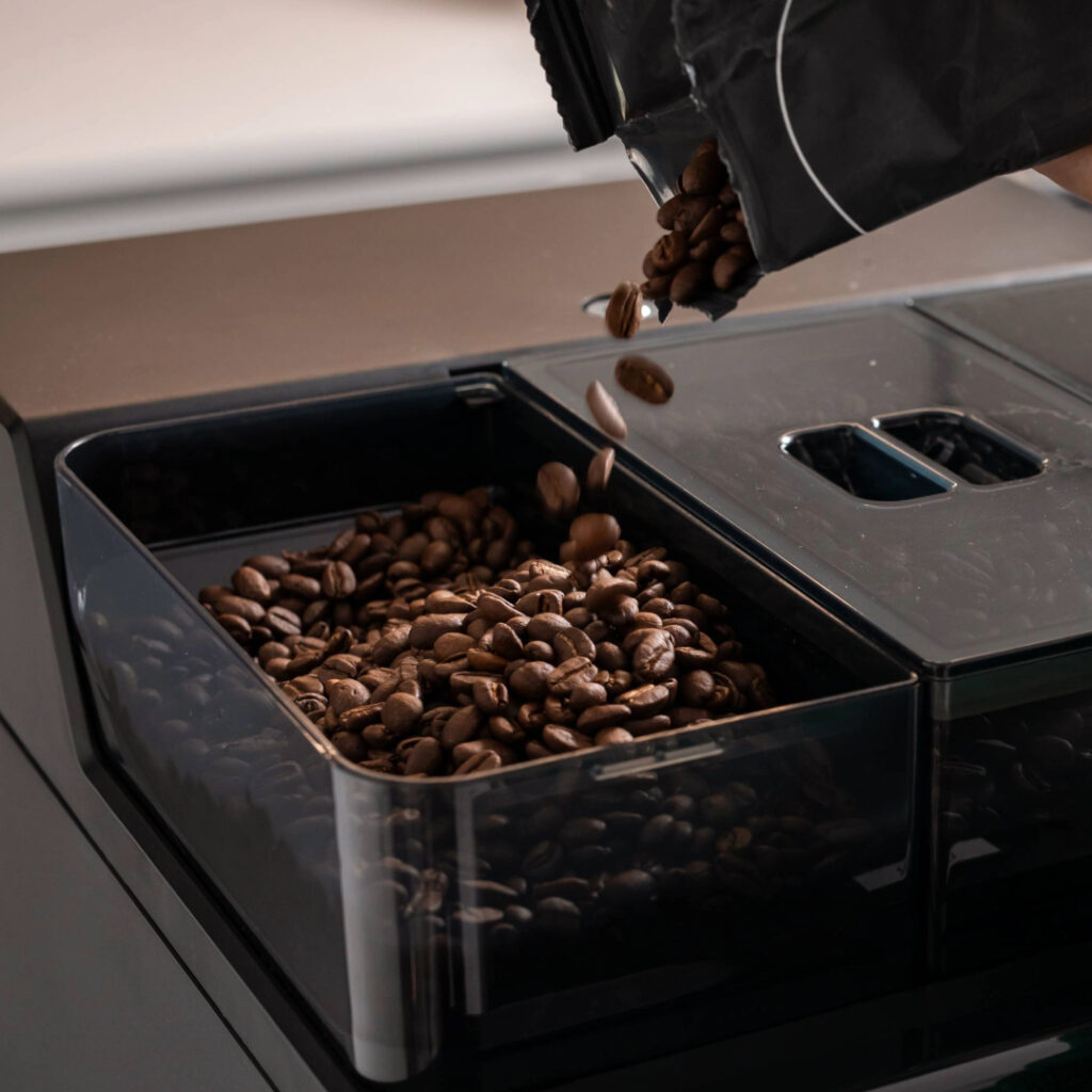Pouring Matthew Algie coffee beans into a bean to cup coffee machine hopper