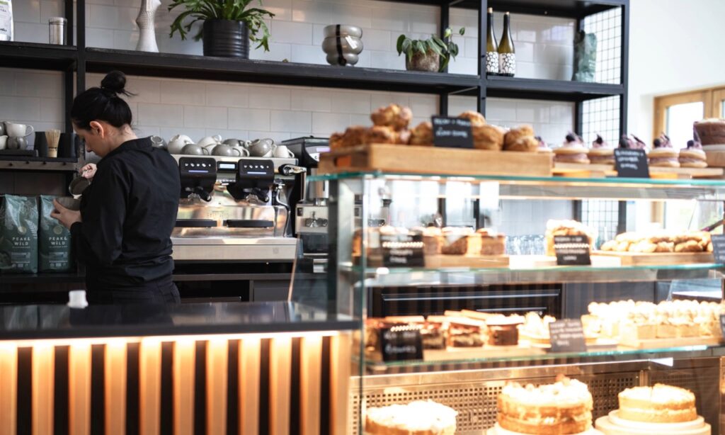 Cafe setup with counter and cake display, barista making a coffee with a traditional coffee machine